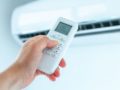 Osoba ustawiająca temperaturę klimatyzacji pilotem w domu podczas upału