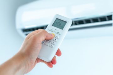 Osoba ustawiająca temperaturę klimatyzacji pilotem w domu podczas upału